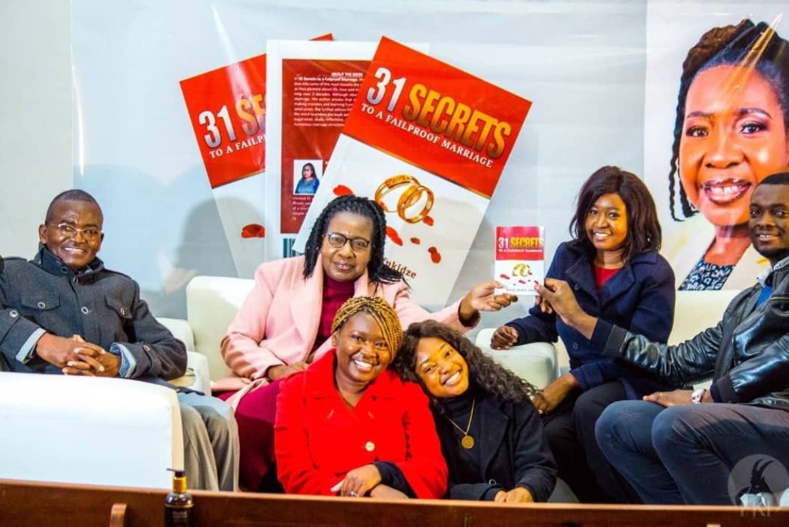 Guests seated together at the launch of 31 Secrets to a Failproof Marriage, holding a copy of the book beneath promotional banners.