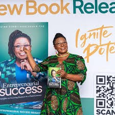 Divine Simbi-Ndhlukula holding her book Entrepreneurial Success at its launch, beside a banner showing the cover.