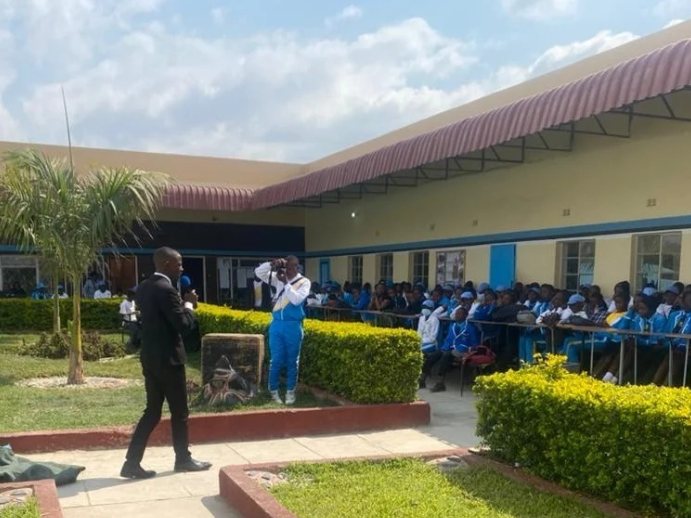 A TisuMazwi facilitator addressing pupils at an outdoor school assembly.