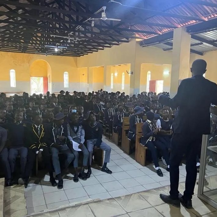 A TisuMazwi facilitator addressing a packed school hall of uniformed students.