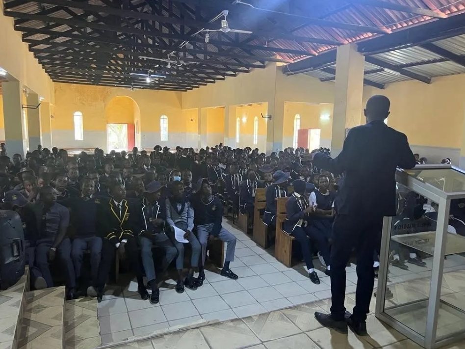 A TisuMazwi facilitator addressing a packed school hall of uniformed students.